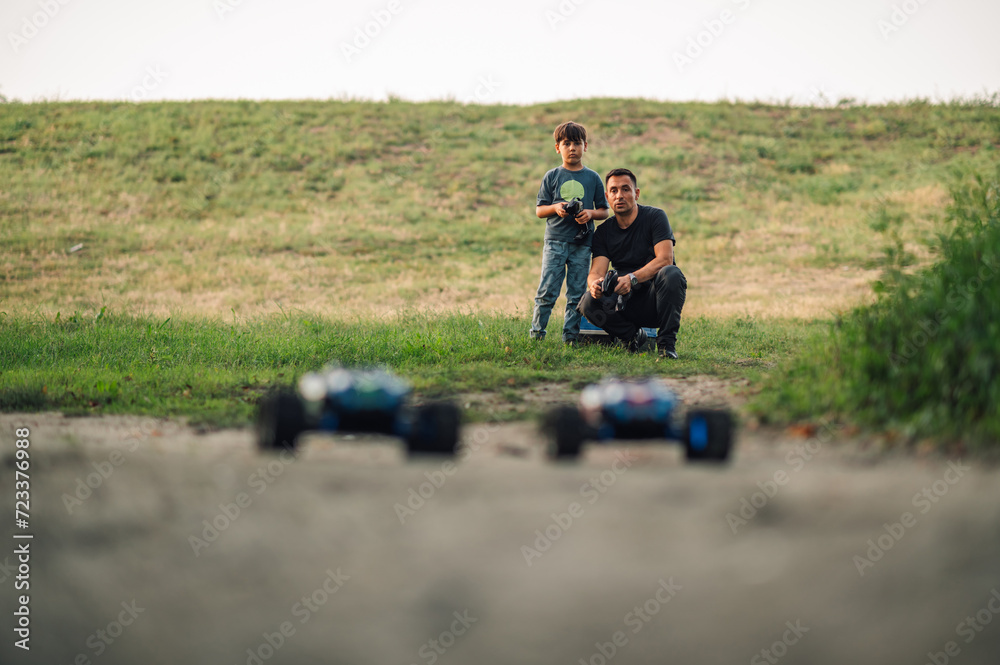 Father and son playing with toy cars in nature, cars in blurry background.
