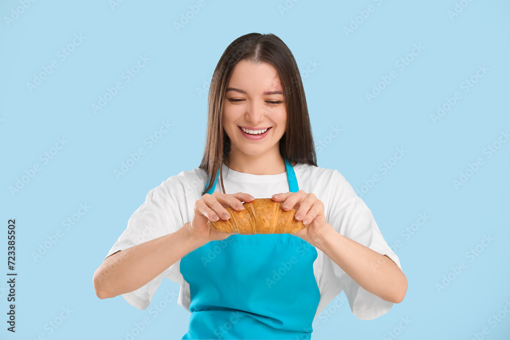 Pretty young woman in apron with fresh croissant on blue background Pretty young woman in apron with fresh croissant on blue background