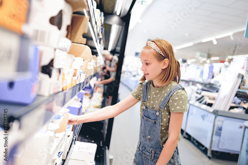 Pretty girl child choosing yogurt in supermarket. Beautiful female preteen kid looking milk products in grocery store photo