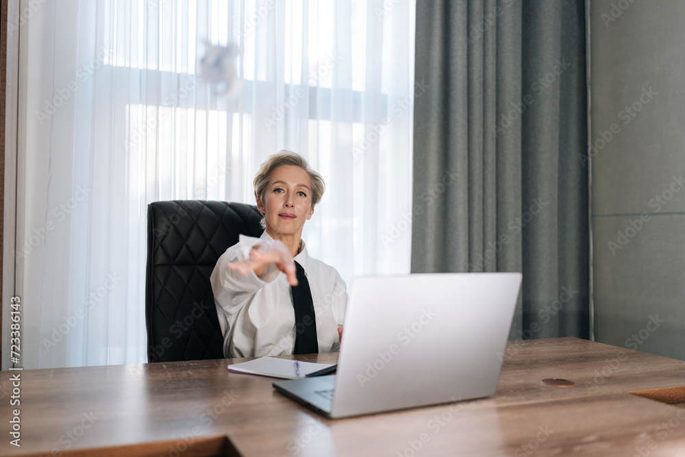 Portrait of displeased middle-aged female boss sitting in office desk, gesturing with hand at someone, looking at camera. Stressed female entrepreneur expressing disappointment by bending forward. Portrait of displeased middle-aged female boss sitting in office desk, gesturing with hand at someone, looking at camera. Stressed female entrepreneur expressing disappointment by bending forward.