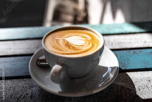 Cappuccino Tassen aus Porzellan in einem Café bei Sonnenschein auf einem Holztisch im Freien mit Herzsymbol