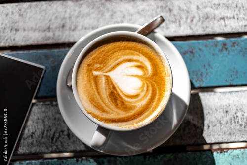 Cappuccino Tassen aus Porzellan in einem Café bei Sonnenschein auf einem Holztisch im Freien mit Herzsymbol