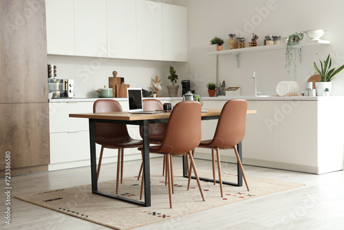 Wooden table with laptop, tea set and notebook in interior of modern kitchen