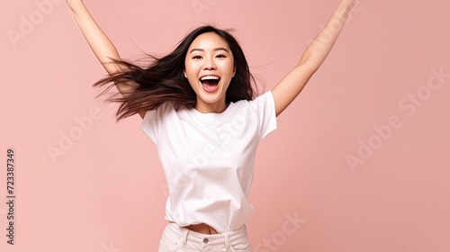 Young Asian woman with a happy expression in a white t-shirt on her face, is very happy with something excited, smiling and with her arms raised in the air on isolated background. photo