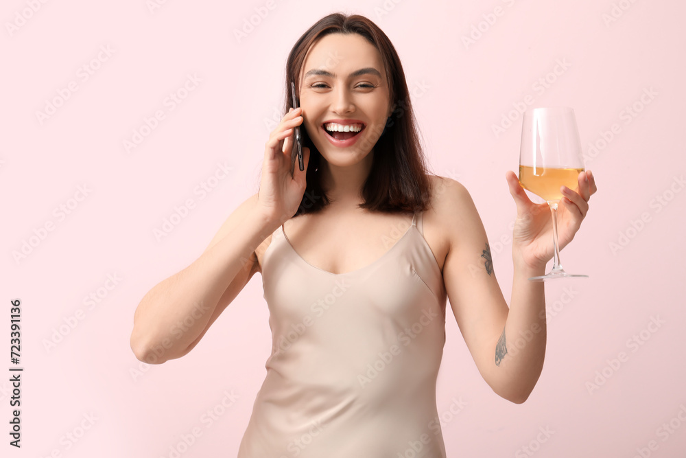 Beautiful young woman with glass of white wine talking by mobile phone on pink background Beautiful young woman with glass of white wine talking by mobile phone on pink background