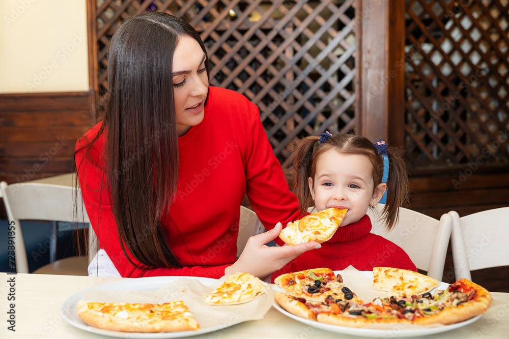 little girl eats pizza close up from parent's hand. Happy mother and daughter eat pizza in a cafe and having fun. Happy family concept. Fast food little girl eats pizza close up from parent's hand. Happy mother and daughter eat pizza in a cafe and having fun. Happy family concept. Fast food