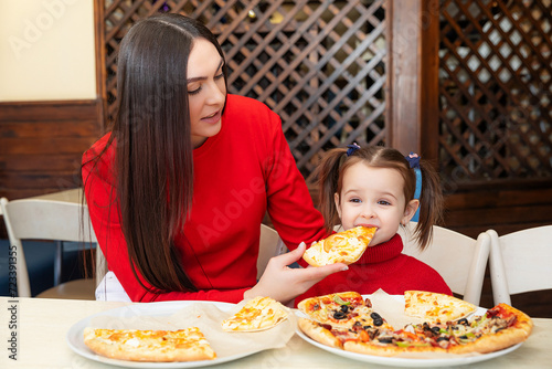 little girl eats pizza close up from parent's hand. Happy mother and daughter eat pizza in a cafe and having fun. Happy family concept. Fast food