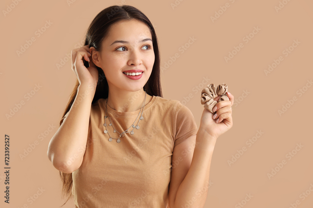 Young Asian woman with scrunchy on beige background Young Asian woman with scrunchy on beige background