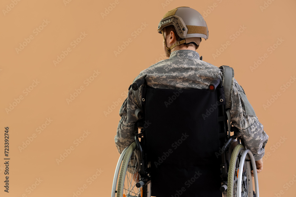 Male soldier in wheelchair on beige background, back view