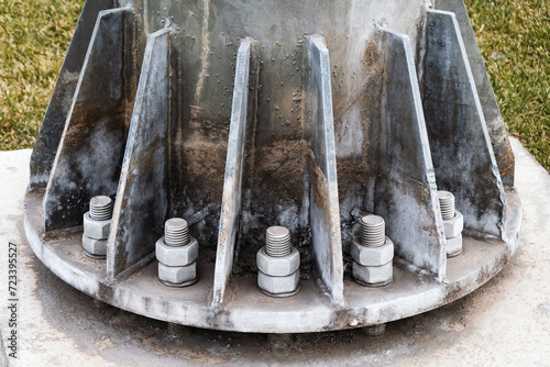 Base of metal billboard column attached to concrete foundation with bolts and nuts, close-up of the metal detayl