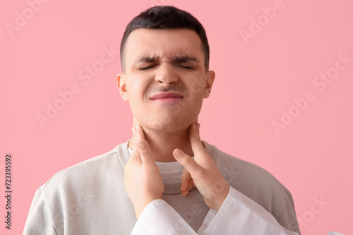 Endocrinologist examining thyroid gland of young man on pink background, closeup photo