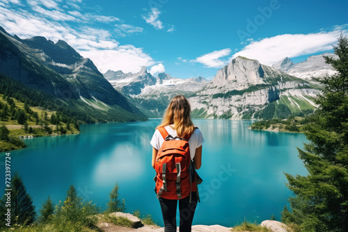 Travel background concept. The back view of the woman looking and the beautiful landscape with the lake or the river, mountains covered in snow, trees in the summer
