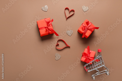 Small shopping cart with gift boxes and hearts on brown background. Valentine's Day celebration