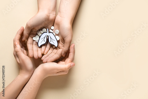 Hands of woman and child with paper lungs and pills on beige background photo