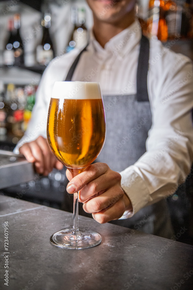 Camarero sirve una cerveza de un grifo en una barra de bar en una copa de cristal