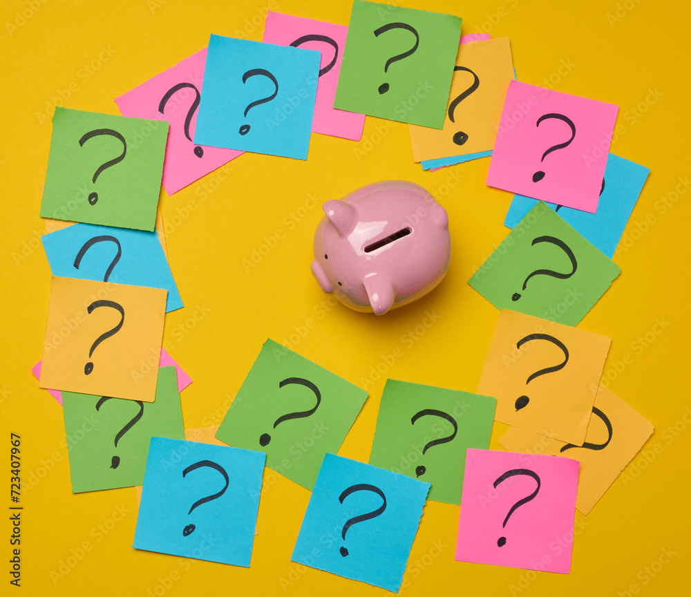 Ceramic piggy bank and stickers with drawn question marks on a yellow background, top view Ceramic piggy bank and stickers with drawn question marks on a yellow background, top view