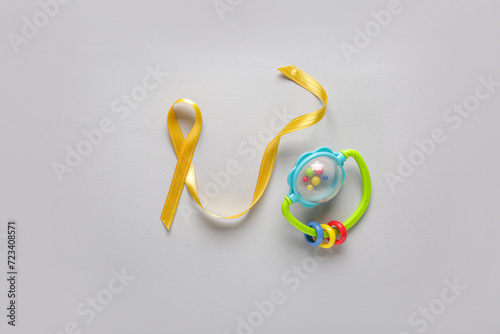 Golden ribbon with baby rattle on white background. Childhood cancer awareness concept