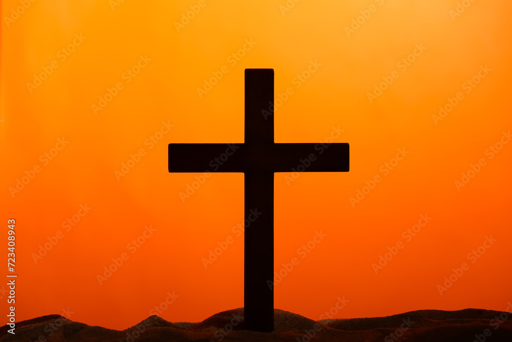 Wooden cross on sand against orange background. Good Friday concept