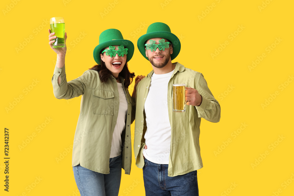 Φωτογραφία Happy young couple in leprechaun hats with glasses of beer on yellow background