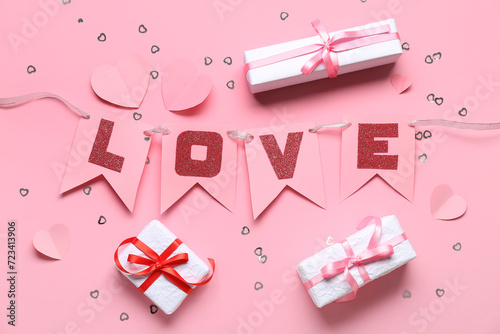 Garland made of paper flags with word LOVE and gift boxes on pink background. Valentine's Day celebration