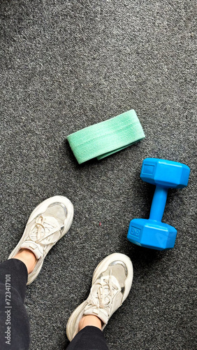 Top View: Girl's legs in sporty sneakers next to a dumbbell. Perfect shot for sport and fitness-related concepts