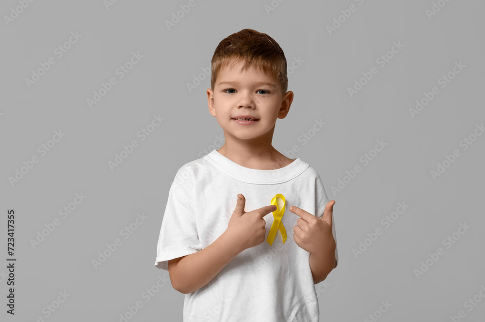 Cute little boy pointing at yellow ribbon on grey background. International Childhood Cancer Day Cute little boy pointing at yellow ribbon on grey background. International Childhood Cancer Day