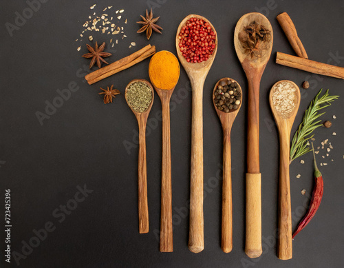 Spices in wooden spoons on a black background with free space for writing on the edge