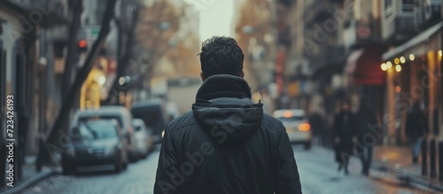 Man in black jacket walking alone on city street from behind in slow motion. photo