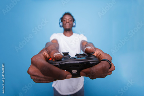 African american male individual wearing a headset and using a controller to play video games. Young black man playing a game with a joystick while listening to music with headphones.