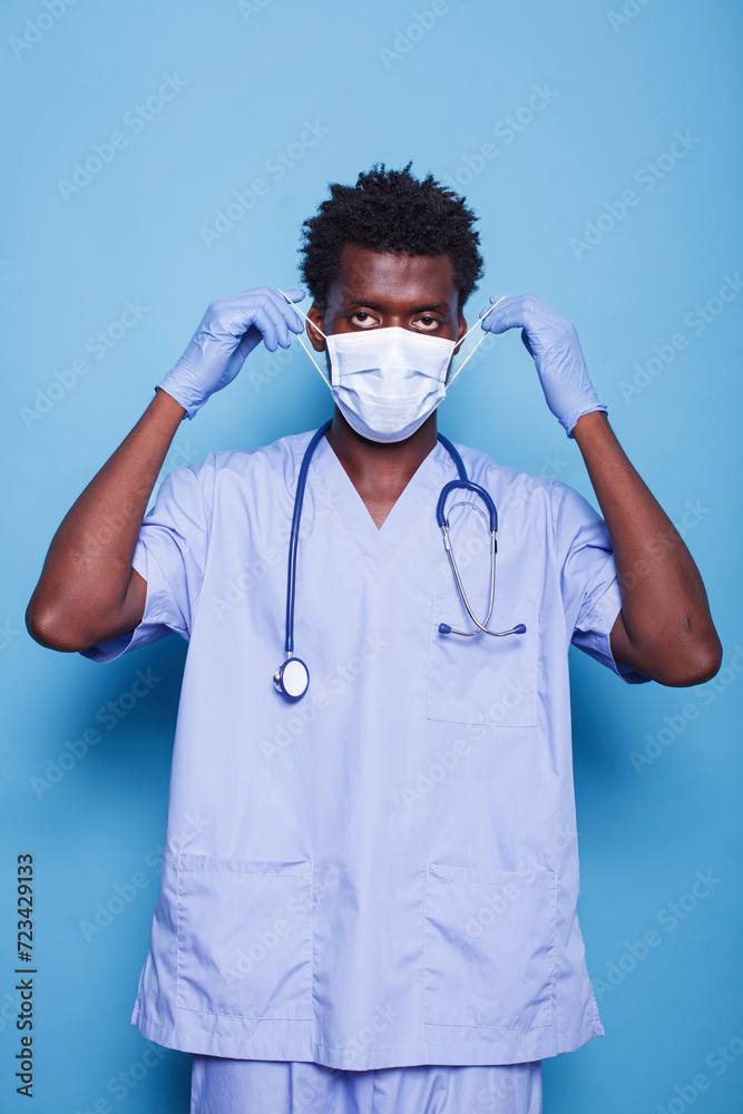 Portrait of a medical specialist putting on face mask to defend against the covid 19 epidemic. Man with blue scrubs, stethoscope, and gloves staring at camera, working as a nurse. Portrait of a medical specialist putting on face mask to defend against the covid 19 epidemic. Man with blue scrubs, stethoscope, and gloves staring at camera, working as a nurse.