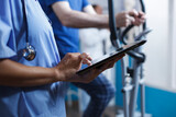 Doctor in blue scrubs and a stethoscope is closely examining a healthcare report on digital device at a hospital. Close-up of female medical specialist surfing the net with her tablet.