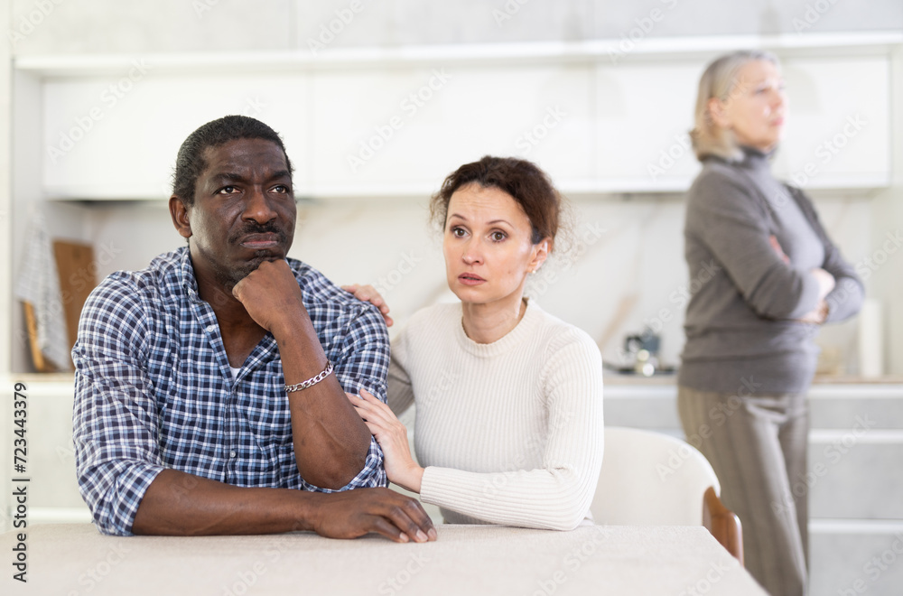 Fototapeta premium Wife calms husband down during family quarrel with mother-in-law
