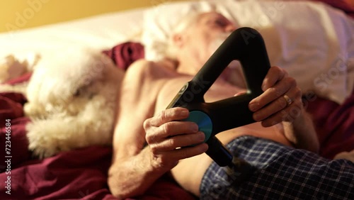 Elderly man massages with percussion therapy massage gun to relieve pain of muscle aches after workout. Warming up muscles with hand held massager. photo