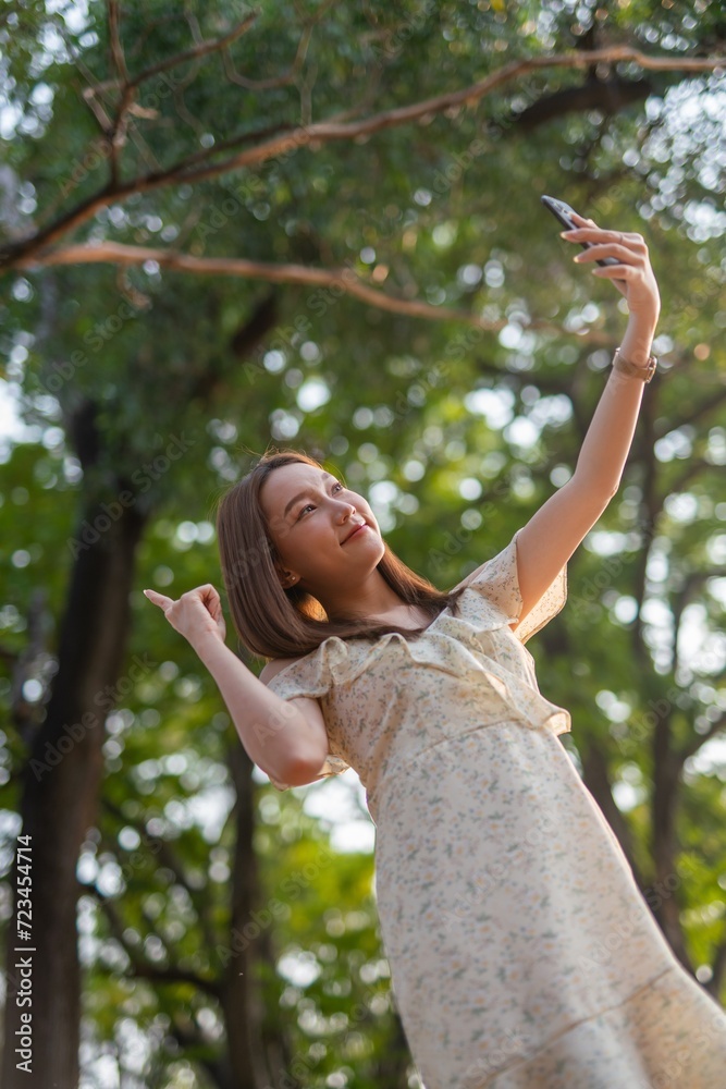 Beautiful woman using phone in a greenery park during sunset Beautiful woman using phone in a greenery park during sunset