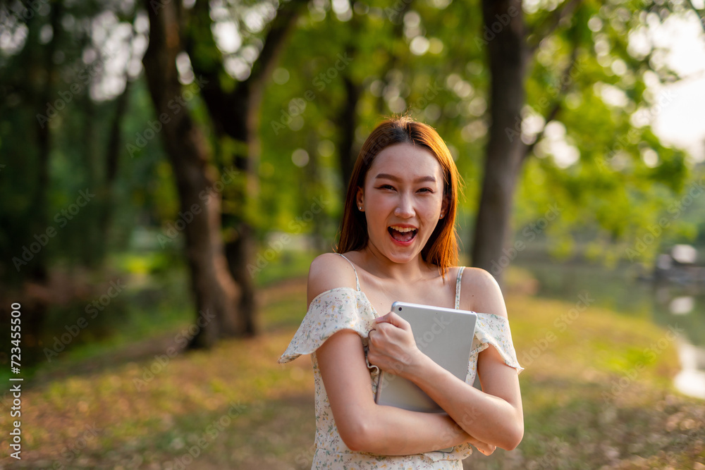 Beautiful Young Asian Woman Finds Serenity, Nature, and Inspiration While Holding a Digital Tablet in the Sunset Breeze at the Park Beautiful Young Asian Woman Finds Serenity, Nature, and Inspiration While Holding a Digital Tablet in the Sunset Breeze at the Park