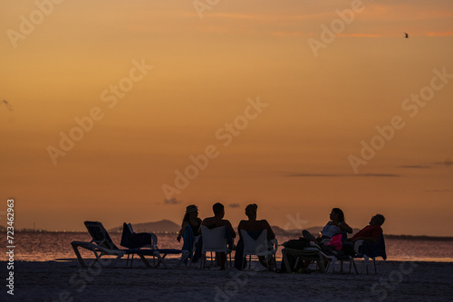 Grupo de personas sentadas conversando mientras observan el atardecer en la playa de una isla en Venezuela photo