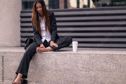 Business woman sitting on the street with foot pain. heels and formal suit massages her feet.