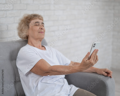 An elderly Caucasian woman suffers from farsightedness and tries to read a message on a smartphone with her arm outstretched.  photo