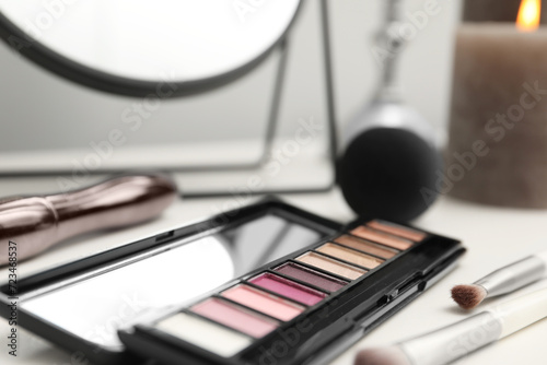 Mirror, cosmetic products and burning candle on dressing table, closeup