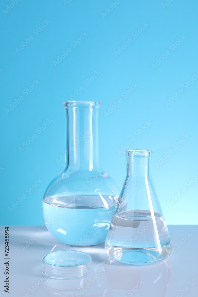 Laboratory analysis. Glass flasks on table against light blue background Laboratory analysis. Glass flasks on table against light blue background