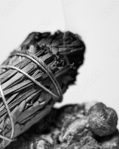 B & W Burning California White Sage and Sweetgrass Ceremonial Herb Bundle Resting on Rough Natural Green Prehnite Crystal Gemstone Mineral Against a White Backdrop