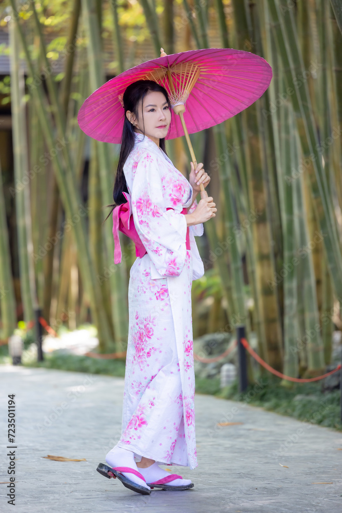 Asian woman wear Japanese kimono holding umbrella walking in the bamboo forest.Woman in Kimono dress enjoying,walking on street outdoors in slow motion.Beautiful Woman standing on street.