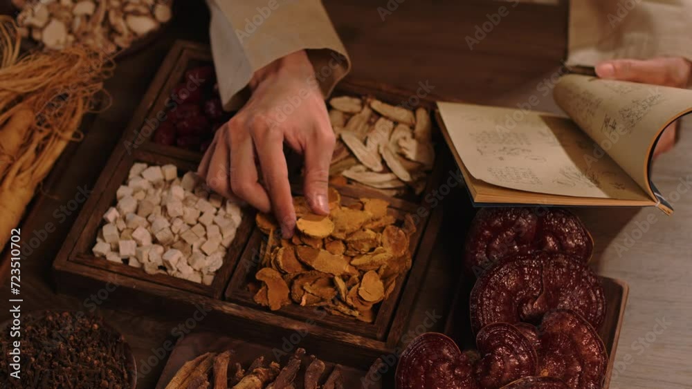 Oriental medicine concept. Ganoderma mushrooms, ginseng, jujube, licorice and other dried medicinal herbs are stored in wooden trays. The physician is studying information from ancient books.