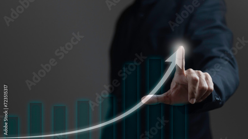 Business growth concept. Businessman uses index finger with glowing arrow tip on graph showing business growth on dark background. photo