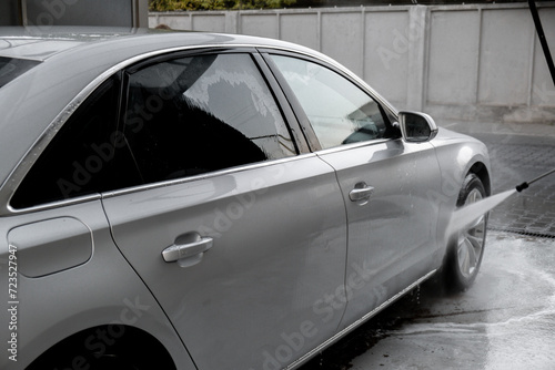 Washing luxury silver car on touchless car wash. Washing sedan car with foam self-service and high pressure water. Winter cleaning in car wash. Cleanliness environment