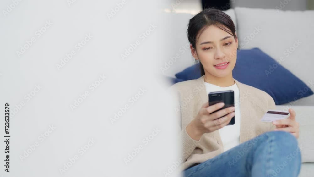 Young asian woman sitting on sofa in living room, makes online banking payments through the internet from bank card on smartphone. Shopping online on mobile phone with credit card Young asian woman sitting on sofa in living room, makes online banking payments through the internet from bank card on smartphone. Shopping online on mobile phone with credit card