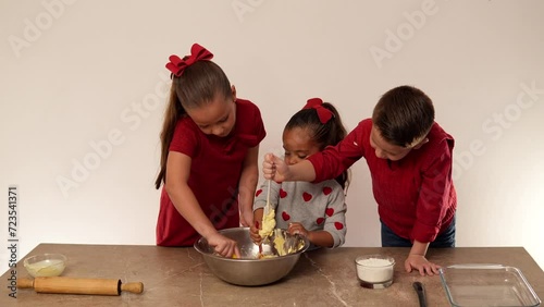 Niños hermanos amigos felices preparando y mezclando mantequilla con harina para hacer unas ricas galletas y compartirlas con su familia ayudandose photo