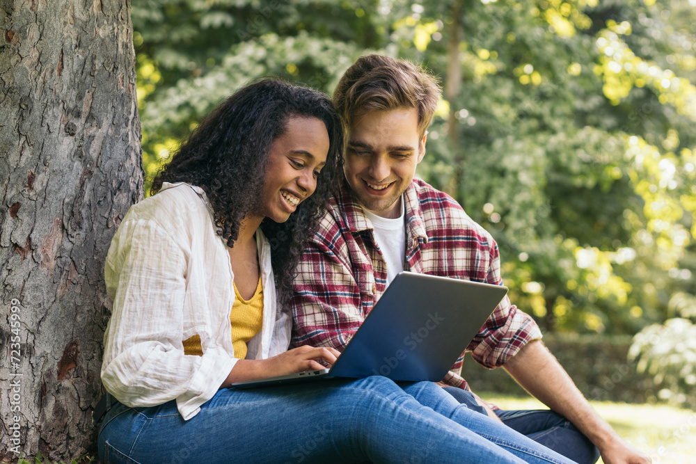 Multiracial couple studying in the park with laptop Multiracial couple studying in the park with laptop