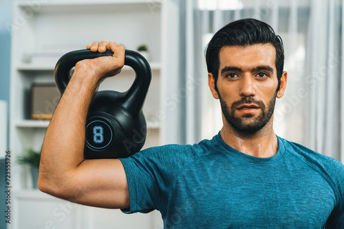 Athletic body and active sporty man lifting kettlebell weight for effective targeting muscle gain at gaiety home as concept of healthy fit body home workout lifestyle.