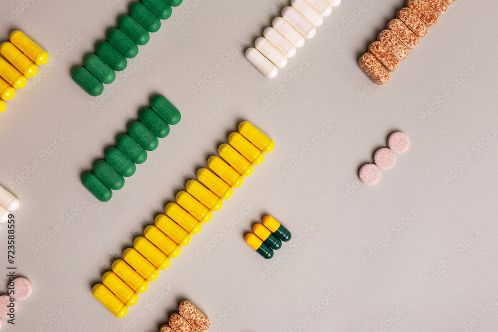 Different colored tablets and pills are laid out in a line on a light background top view. Different colored tablets and pills are laid out in a line on a light background top view.